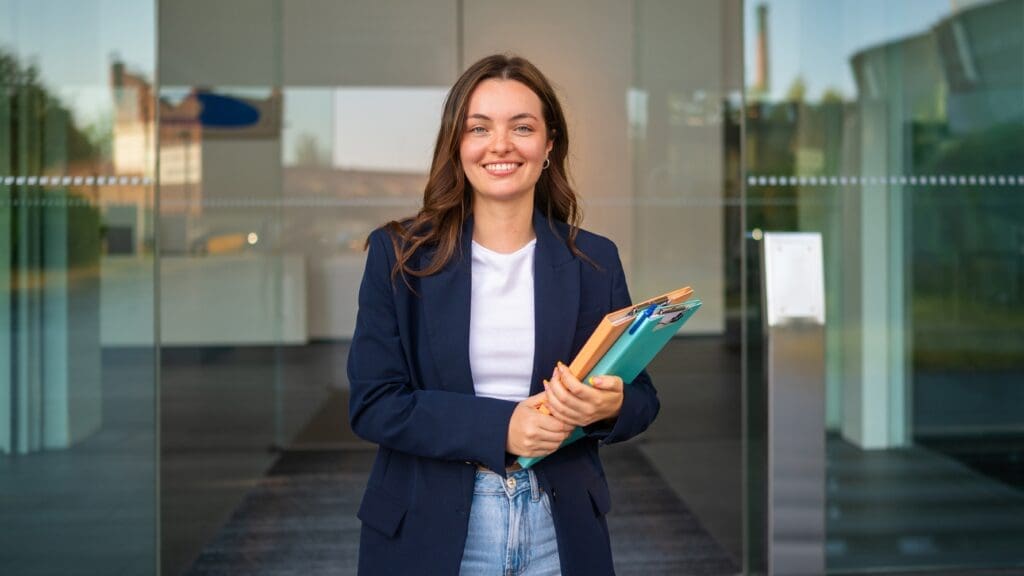confident,young,businesswoman,holding,folders,smiling,at,office,entrance confident,young,businesswoman,holding,folders,smiling,at,office,entrance
